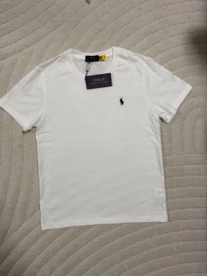 Ralph Lauren T-shirt  - Klassisk vit t-shirt från Polo Ralph Lauren med rund hals och korta ärmar. T-shirten har den ikoniska broderade loggan på bröstet och är tillverkad i mjuk bomull för en skön känsla. Perfekt basplagg som funkar till allt. Fint skick 