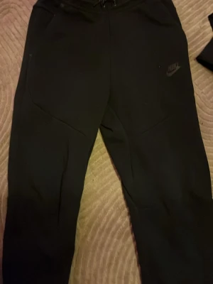 Nike Tech Fleece  - Säljer ett par svarta mjukisbyxor från Nike i storlek XS. Byxorna har dragsko i midjan, två sidofickor och Nike-logga på vänster ben. Perfekta för chill eller träning, riktigt sköna och stilrena.
