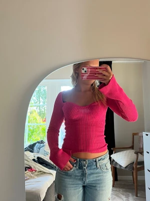 Ribbad rosa croppad topp - Trendig ribbad topp i stark rosa färg med croppad passform och långa ärmar. Toppen har en snygg v-ringad urringning och sitter tight. 