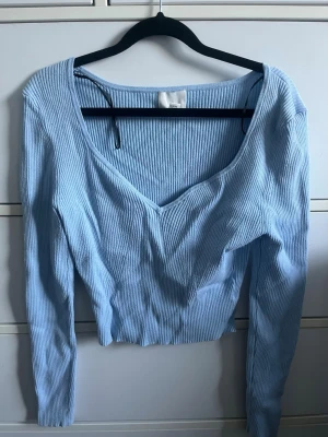 Ljusblå ribbad topp med v-ringning - Trendig ljusblå långärmad topp i ribbat material med djup v-ringning framtill. Toppen har en kroppsnära passform och är något croppad i modellen. Perfekt att matcha med jeans eller kjol för en snygg vardagslook.