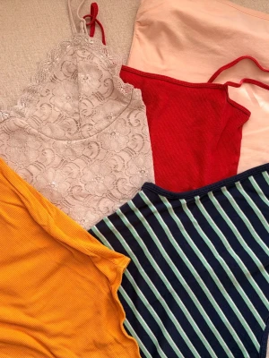 5 toppar i olika färger - Säljer ett paket med fem toppar: ett beige spetslinne, ett ribbat rött linne, en ribbad senapsgul body, en aprikos bandeu topp och ett marinblått linne med gröna och vita ränder. Perfekta för sommaren och att mixa och matcha till olika outfits. Första ägare. Storlek XS, S se bilder