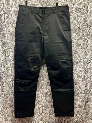 Svarta cargobyxor från Stone Island - Säljer ett par svarta cargobyxor från Stone Island med raka ben och flera fickor, inklusive dragkedjeficka fram och bakfickor med knapp. Byxorna har den klassiska Stone Island-loggan bak och är tillverkade i ett slitstarkt bomullsmaterial.