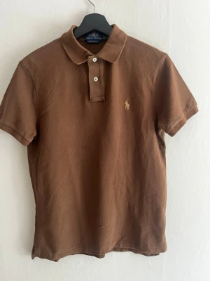 Brun pikétröja från Polo Ralph Lauren - Klassisk brun pikétröja från Polo Ralph Lauren. En riktigt snygg Piké. Hör gärna av er!