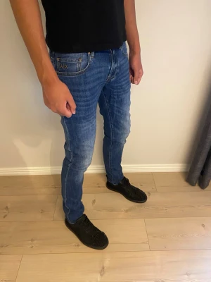 Blå slim fit jeans från Armani Exchange - Snygga blå slim fit jeans från Armani Exchange med klassisk femficksmodell och diskret logga på bakfickan. Jeansen har en lätt tvättad look och smal passform som sitter tajt längs benen. Perfekta för en trendig och avslappnad stil.