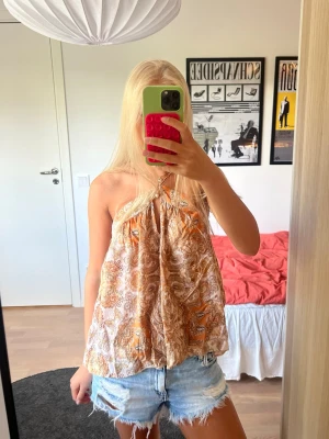 Orange mönstrad halternecktopp - Orange/beige mönstrad sommartopp som är halterneck i luftig passform🧡🧡Ärmlös därmed perfekt för varma dagar och sommaren! Axelbanden är justerbara. Tyget är lite slitet på ett ställe, skriv för bilder. Materialet är lyocell och viskos.