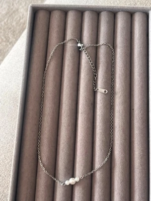 Silverhalsband med tre pärlor - Snyggt och minimalistiskt halsband i silverfärgad metall med tre små vita pärlor i mitten. Kedjan är tunn och har ett justerbart lås för perfekt passform. Perfekt accessoar för dig som gillar stilrena smycken med en elegant touch.