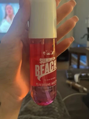 Summer Beach Perfume Mist 100ml - Fräsch parfymmist med tropisk doft i en cylinderformad plastflaska. Flaskan är rosa med vit kork och har texten 'SUMMER BEACH' på framsidan. Perfekt att spraya i håret eller på kroppen för en somrig känsla.