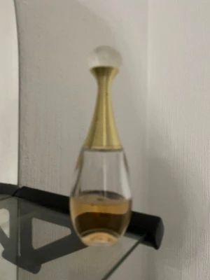 Dior parfyn - Säljer en elegant parfymflaska i droppform med guldigt hals och transparent glas. Flaskan har en rund, frostad kork och innehåller en ljusgul vätska. Perfekt för dig som gillar lyxig design och vill ha en snygg detalj på sminkbordet.