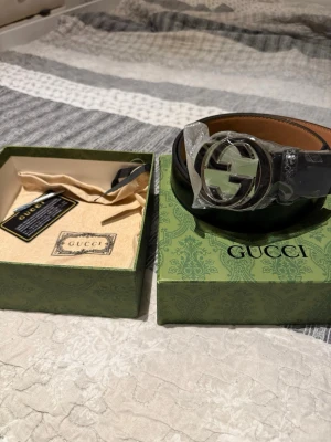 Svart skärp med silverdetalj från Gucci - Snyggt svart skärp från Gucci med klassiskt GG-spänne i silverfärg. Skärpet har en stilren design och kommer i originalförpackning med dustbag och certifikat. Perfekt accessoar för att lyfta vilken outfit som helst. Helt oanvänd och redo att skickas. Priset går att diskutera vid snabb köp🫡