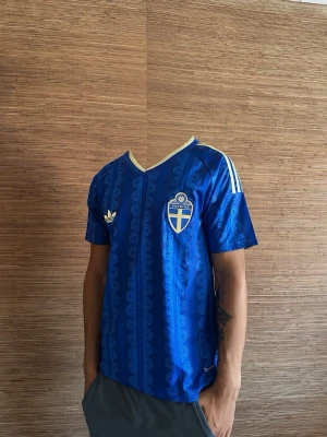 Svergie Vm tröja - Säljer en Sverige Vm tröja från Adidas med Sveriges landslagsemblem på bröstet. Tröjan har gula detaljer, v-ringad krage och klassiska Adidas-ränder på axlarna. Materialet är lätt och andas, perfekt för allt 