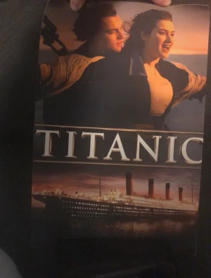 Titanic film poster - Snygg poster med motiv från filmen Titanic. Affischen har en ikonisk bild på huvudkaraktärerna mot en solnedgång och texten 'TITANIC' samt en bild på skeppet. Perfekt för filmälskare eller som dekoration i rummet.