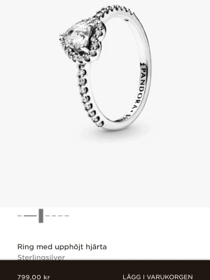 Pandora ring med hjärtformad sten - Snygg ring från Pandora i sterlingsilver med en upphöjd hjärtformad klar sten i mitten. Använd ett fåtal gånger. Antar att storleken är 50 som står på insidan av ringen. Nypris 799kr