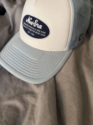 Grå meshkeps från New Era - Säljer en grå keps från New Era med meshmaterial runtom för extra ventilation. Aldrig använd. Kepsen har justerbar snapback och böjd skärm. Perfekt för dig som vill ha en luftig och sportig look. 
