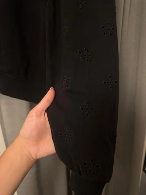 Svart sweatshirt med broderade detaljer - Säljer en svart sweatshirt med puffärmar och broderade blommönster på ärmarna. Tröjan har rund halsringning och muddar vid ärmslut och nederkant. Perfekt för dig som vill ha en basic men ändå unik look. Storlek M men sitter som S