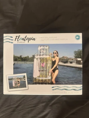 Uppblåsbar parfymflaska från Floatopia - Säljer en stor uppblåsbar badmadrass formad som en parfymflaska från Floatopia. Madrassen är transparent med guldglitter och rosa detaljer, samt ett hjärta på framsidan. Perfekt för poolhäng och strandliv. Tillverkad i slitstark plast och passar för personer över 14 år.