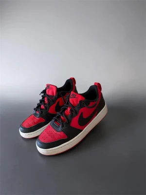 Nike Air Force 1 Low röd/svart storlek 38,5 - Snygga Nike Air Force 1 Low sneakers !STORELK38,5!  i rött och svart med klassisk vit sula och röd undersida. Skorna har en ikonisk siluett, svart swoosh och detaljer i läder. Perfekta för dig som vill sticka ut med en sportig och trendig look.