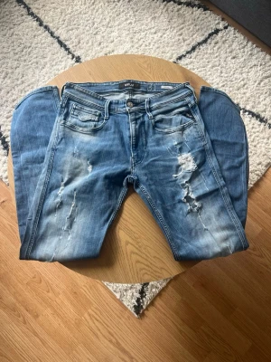 Ljusblå Replay med slitningar  - Tja👋 Säljer ett par blå jeans från Replay med slitningar och hål på framsidan för en trendig look🤩 Storlek är W31 L32 i Anbass modell🧼Jeansen har fem fickor, normal midja och raka ben😮‍💨Materialet är klassisk denim i bomull. Perfekta för dig som gillar en avslappnad och cool stil✌️ Meddela gärna vid frågor📩