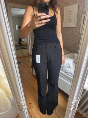 Svarta vida kostymbyxor - Säljer ett par svarta kostymbyxor med hög midja och vida ben. Byxorna har pressveck framtill, bälteshällor och diskreta fickor. Perfekta för en clean och stilren look. Materialet ser ut att vara en mjuk och följsam mix, troligtvis polyester eller viskos.