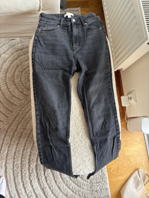 Svarta raka jeans med hög midja - Snygga svarta jeans med raka ben och hög midja. Klassisk femficksmodell med knapp och dragkedja framtill. Jeansen har en stilren look och passar perfekt till en avslappnad streetstyle. Materialet är denim i bomull.