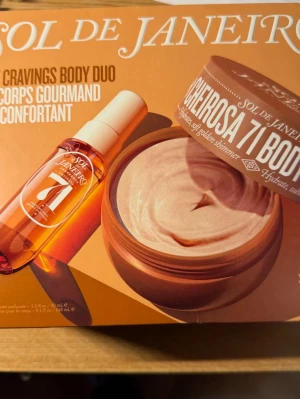 Sol de Janeiro Cozy Cravings Body Duo - Set med kroppsspray och body cream från Sol de Janeiro. Innehåller Cheirosa 71 Body Fragrance Mist och Cheirosa 71 Body Cream med doft av karamelliserade toner. Förpackningen är i varma bruna och orange nyanser. Perfekt för dig som älskar lyxiga kroppsvårdsprodukter.