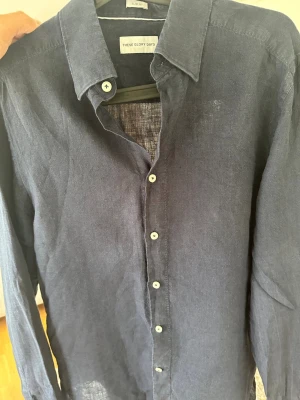 Mörkblå linneskjorta These Glory Days - Snygg mörkblå skjorta från These Glory Days i 100% linne. Skjortan har klassisk krage, knappar framtill och lång ärm. Slim fit-modell som ger en modern och stilren look. 