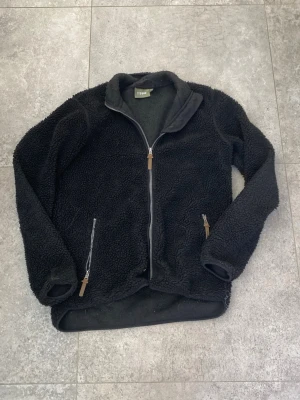 Svart teddyjacka - Mysig svart teddyjacka med hel dragkedja framtill och två sidofickor med dragkedja. Jackan har hög krage och detaljer i fuskläder på dragkedjorna. Använd ett fåtal gånger så i bra skick. Hör av er vid frågor✅