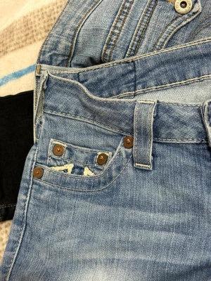 Ljusblå True Religion jeans - As lågmidjade True religion jeans, har två defekter ( kolla bild 3, 5 ) jag är  171 och de kommer ända ner!!! Skriv om ni vill ha mått 