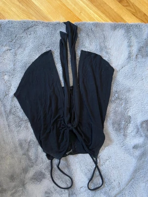 Svart topp från Gina Tricot - Säljer en svart knyttopp från Gina Tricot i mjukt material. Toppen har smala axelband och knytband framtill som ger en snygg och justerbar passform. Perfekt till jeans eller kjol för en trendig look.