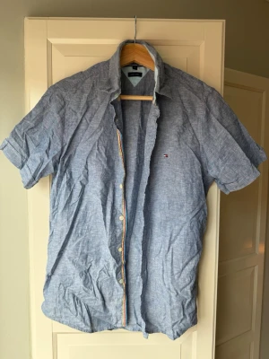Tommy Hilfiger linneskjorta  - Säljer en blå kortärmad linneskjorta från Tommy Hilfiger. Storlek S. Skjortan har klassisk krage, knappar framtill och en liten logga på bröstet. Perfekt för dig som gillar en avslappnad men stilren look.