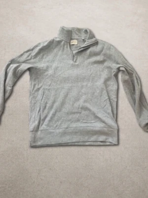Ljusgrå Gant halvzip tröja - En stilren ljusgrå tröja med halv dragkedja och hög krage. Tröjan har långa ärmar och är tillverkad i ett mjukt, tunt material som passar perfekt för lager-på-lager. 