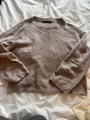 Beige stickad tröja från 157 - Mysig beige stickad tröja från 157 med rund halsringning och långa ärmar. Tröjan har en enkel, rak passform och ribbade muddar vid ärmslut och nederkant. Perfekt för lager på lager under kyliga dagar. Ganska noppig därför priset. 