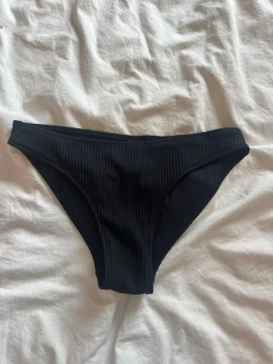 Svarta ribbade bikiniunderdelar - Snygga svarta bikiniunderdelar med ribbad struktur. Klassisk modell med medelhög midja och mjukt, stretchigt material som sitter bekvämt. Perfekta för lata dagar på stranden eller poolen. Använd fåtal gånger.