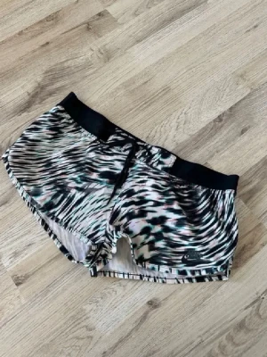 Mönstrade träningsshorts med snörning - Säljer ett par snygga träningsshorts med svartvitt mönster och bred svart midjeresår. Shortsen har snörning framtill och är tillverkade i ett lätt, syntetiskt material som passar perfekt för träning eller sport.