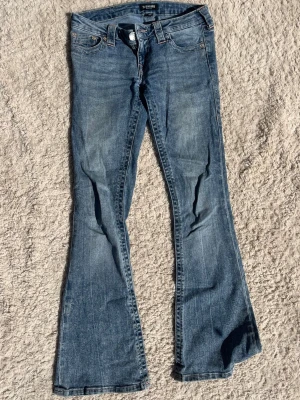 Blå bootcut jeans från True Religion - Säljer ett par blå bootcut jeans från True Religion med broderade bakfickor. Jeansen har låg midja och är perfekta för dig som gillar en avslappnad men trendig stil.