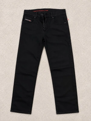 Svarta jeans från Diesel - Snygga svarta jeans från Diesel med raka ben och klassisk femficksdesign. Jeansen har diskreta detaljer och en liten Diesel-logga på myntfickan. Tillverkade i ett mjukt och slitstarkt denimtyg som passar perfekt till din vardagsstil.