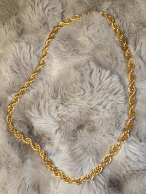 Guldfärgat tvinnat halsband - Snyggt halsband i guldpläterad metall med tvinnad kedja som ger en chunky och trendig look. Halsbandet har en enkel ringlås och glänser fint i ljuset. Perfekt för att lyfta vilken outfit som helst med en touch av lyx.