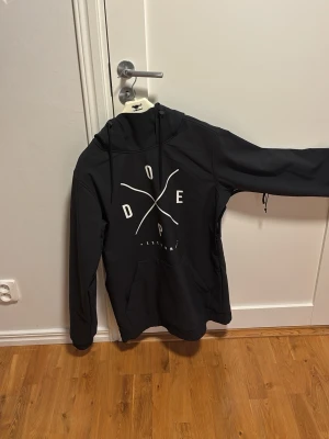 Jacka/skidjacka från dope, nästintill oanvänd - Säljer en svart hoodie från Dope med stor vit logga på bröstet och praktisk magficka. Hoodien har huva med dragsko och långa ärmar. Materialet känns slitstarkt och passar perfekt för en skidtur eller som en vanlig regnjacka eller liknande (pris kan diskuteras vid intresse)