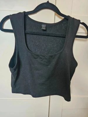 Svart croppad linnetopp från SHEIN - Svart croppad linnetopp från SHEIN  En svart croppad linnetopp från SHEIN med fyrkantig ringning. Toppen är ärmlös och har en enkel, stilren design som passar perfekt till jeans eller kjol. Tillverkad i mjuk bomullsmix för en bekväm känsla.  Kan även hämtas I Partille  E1