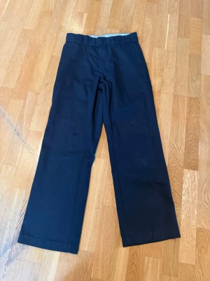 Svarta Dickies 874 chinos - Klassiska svarta Dickies 874 chinos med rak passform och hög midja, går att vika ner så det vita syns så blir de en låg midja, det är så jag använt de. Säljer dessa då de ej passa mig längre och inte använts på länge. Tyvärr så har jag klippt bort lappen med storleken men jag skulle tro att de är storlek 24. 