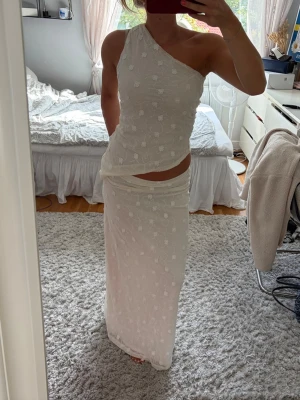 Vit oneshoulder långklänning - Säljer en elegant vit långklänning med oneshoulder-design och diskret blommigt mönster. Klänningen har en smickrande passform och är perfekt för sommarens alla tillfällen. Materialet känns lätt och luftigt.  Nypris för båda delarna: 680kr