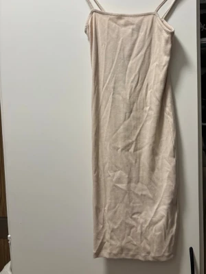 Beige ribbad klänning från Amisu - Säljer en beige ribbad klänning från Amisu med smala axelband och rak passform. Klänningen är enkel och stilren, perfekt för varma dagar. Materialet är mjukt och stretchigt, vilket gör den bekväm att bära.