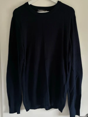 Mörkblå stickad tröja Dressmann - Mörkblå stickad tröja från Dressmann i storlek M. Tröjan har rund halsringning, lång ärm och ett diskret rutmönster i stickningen. Perfekt för lager på lager och enkel att matcha med olika outfits.