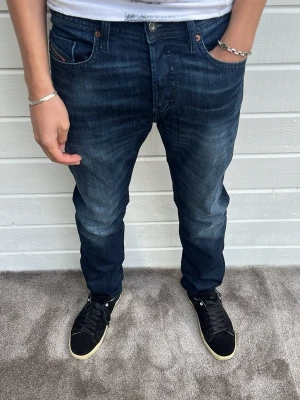 Diesel jeans marinblå - Hej! Säljer dessa riktigt snygga och nästintill nya Diesel jeansen! Modellen på bilden är 183cm och väger 68kg. Passformen på jeansen heter ”Buster” som är Regular slim-tapered. Storlek: W30/L32. Väldigt fin kvalitet! 98% bomull och 2% elastan. Varmt välkommen att höra av dig vid minsta intresse! 