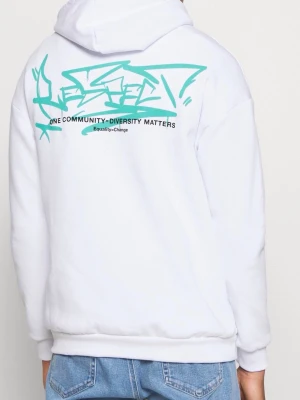 Vit hoodie med turkos graffiti-tryck - Säljer en vit hoodie med huva och dragsnören. På ryggen finns ett stort turkost graffiti-inspirerat tryck och texten 'One Community - Diversity Matters'. Framtill finns en liten text i samma stil. Perfekt för dig som gillar streetwear och vill sticka ut. Liten fläck i fram se bild