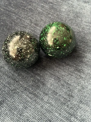 Två svarta och gröna stressbollar - Säljer två runda stressbollar i svart med gröna och vita stänk. De är blanka och har en cool galaxliknande look. Perfekta att ha på skrivbordet eller ta med i väskan för att slappna av när du behöver.
