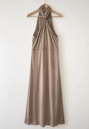 VILA ny - Beige långklänning med halterneck - Elegant beige långklänning i ett mjukt, glansigt material med halterneck och draperad överdel. Klänningen har en stilren siluett och är ärmlös, perfekt för en chic look.
