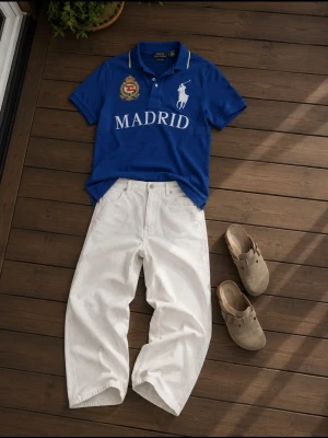 Blå pikétröja från Ralph Lauren - Snygg blå pikétröja från Ralph Lauren med vit text 'MADRID' och broderade detaljer på bröstet. Klassisk krage, knappar framtill och vit logga. Perfekt för dig som gillar sportig och stilren look.