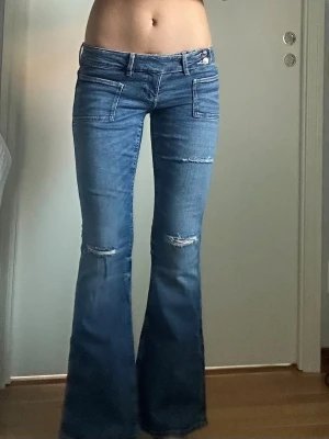 Lågmidjade jeans från Gina Tricot - Lågmidjade jeans med hål från Gina Tricot i storlek M (14+), använt endast fåtal gånger💕. Jeansen heter Pleated flared jeans Midjemått: ca 80 cm Innerben: ca 80 cm Ytterben: ca 96.5 cm  Skriv gärna vid frågor och priset kan alltid diskuteras💕