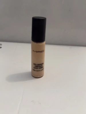 MAC Pro Longwear Concealer ljus - MAC Pro Longwear Concealer i en ljus beige nyans. Kommer i en liten cylinderformad flaska med svart lock. Perfekt för att täcka mörka ringar och ojämnheter. Flytande formula som ger ett naturligt resultat.