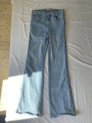 Ljusblå bootcut jeans mid waist  - Säljer ett par ljusblå jeans med bootcut-modell och medelhög midja. Jeansen har klassiska fickor, bälteshällor och dragkedja med knapp. Perfekta för en avslappnad och trendig look. 